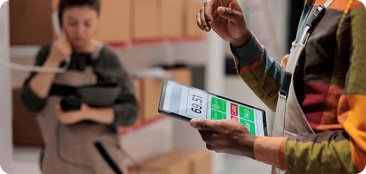 Worker using a tablet to track inventory with stock status indicators in a warehouse setting.